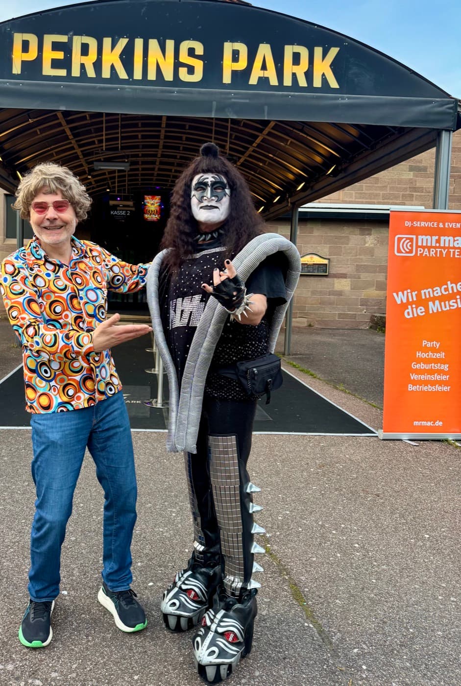 Partygast im KISS-Kostüm mit Plateaustiefeln neben DJ mr. mac vor dem Eingang des Perkins Park Stuttgart
